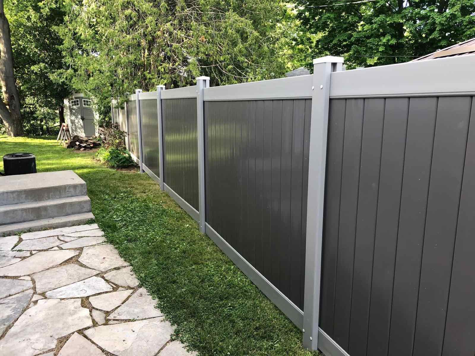 Grey vinyl privacy fence with white posts along a backyard flagstone path