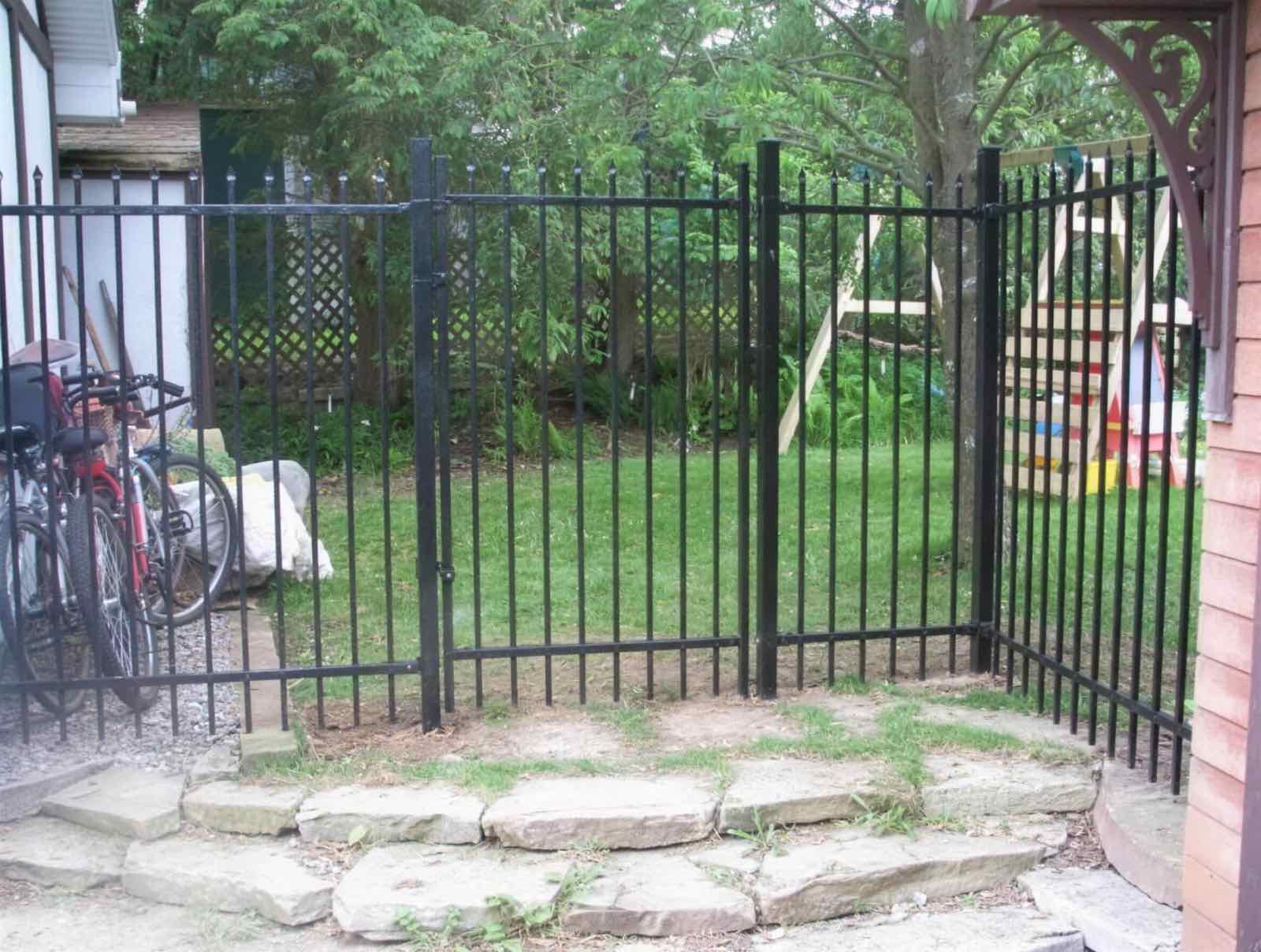 Black iron fence and gate closing off a side yard above stone steps