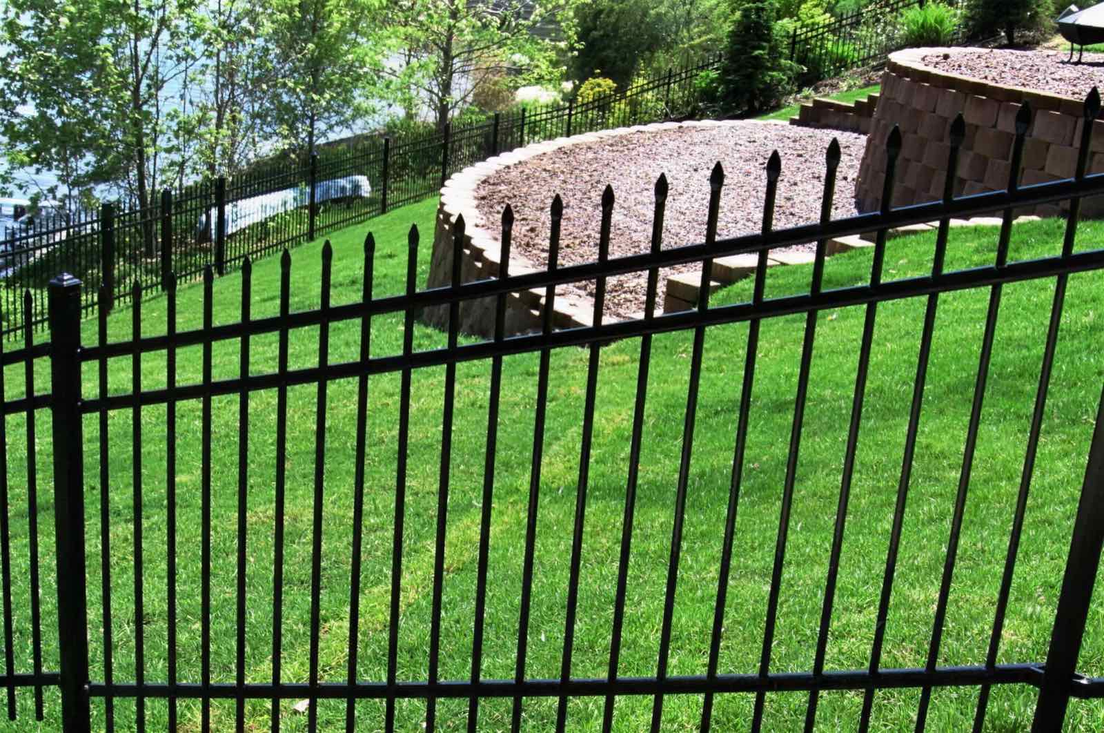 Black ornamental iron fence running down a sloped, terraced lakeside lawn
